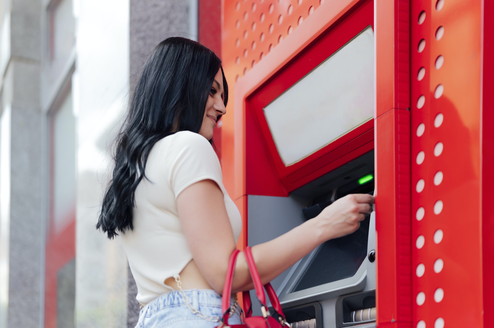Happy brunette woman withdrawing money from credit card at ATM
